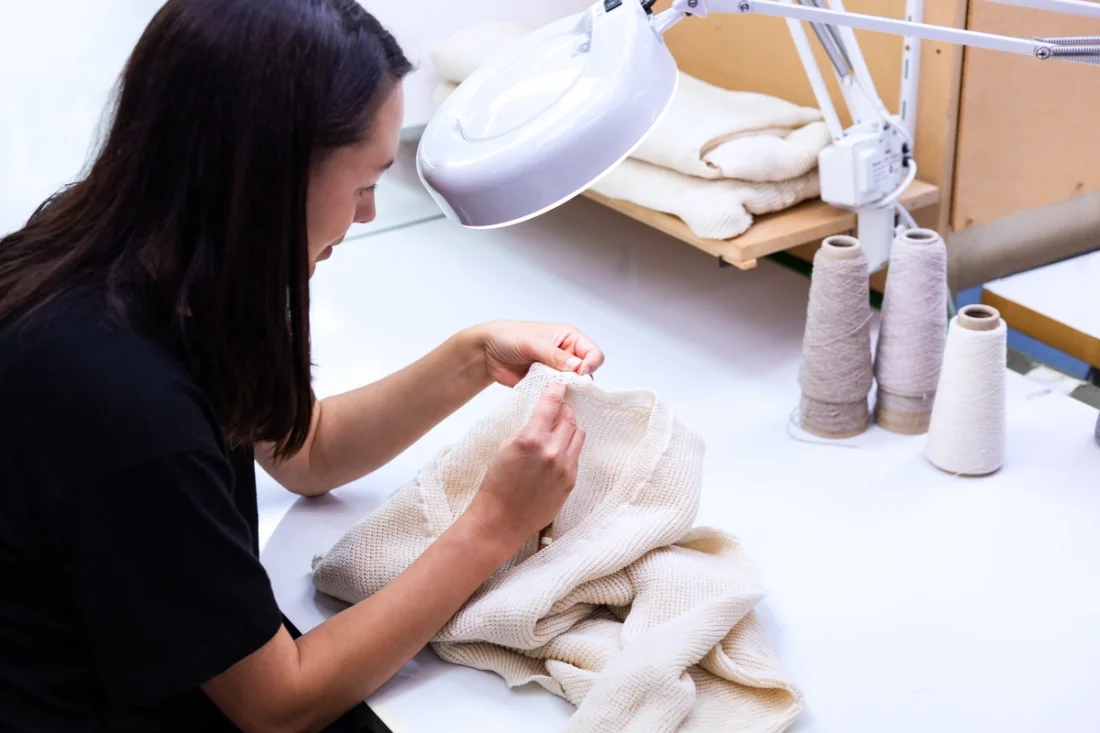 Handstitching a white Untouched World knit sweater.